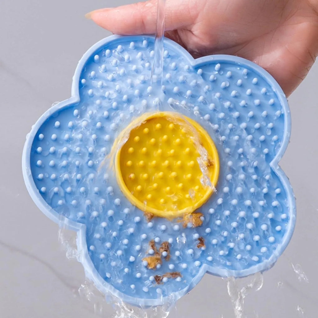 Flower-shaped silicone pet licking mat in blue with suction cups on the back, shown on a tiled surface.