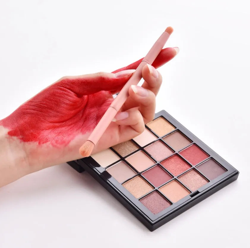 Ten wooden-handle make-up brushes for face and eye application in a pink travel case.