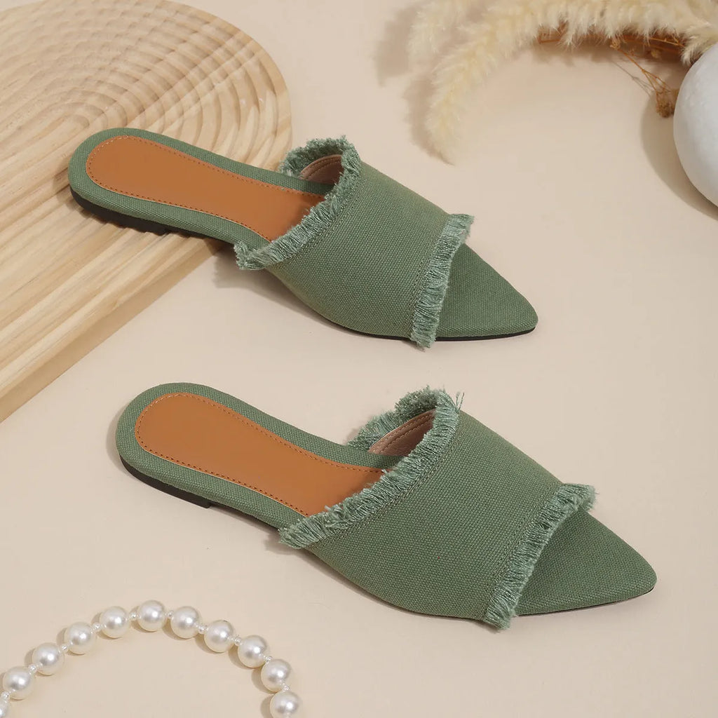 Women's apricot denim flat slippers with tassel detail on a grey background.