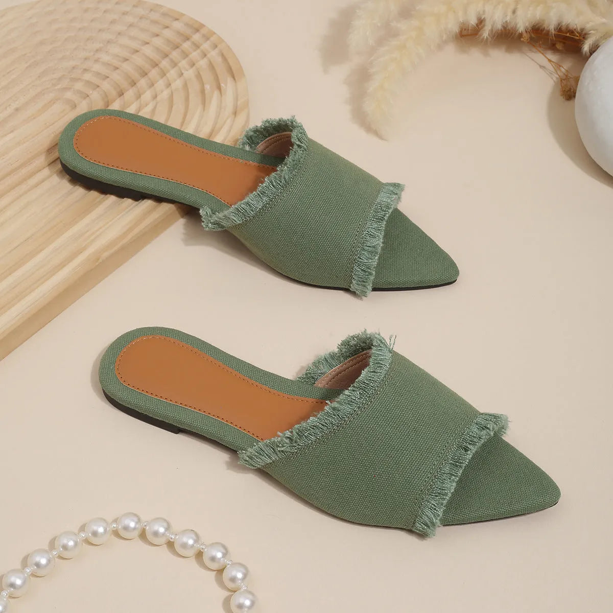 Women's apricot denim flat slippers with tassel detail on a grey background.