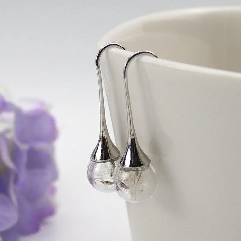 Close-up of transparent glass ball earring with crystal dandelion seed design on a silver hook.
