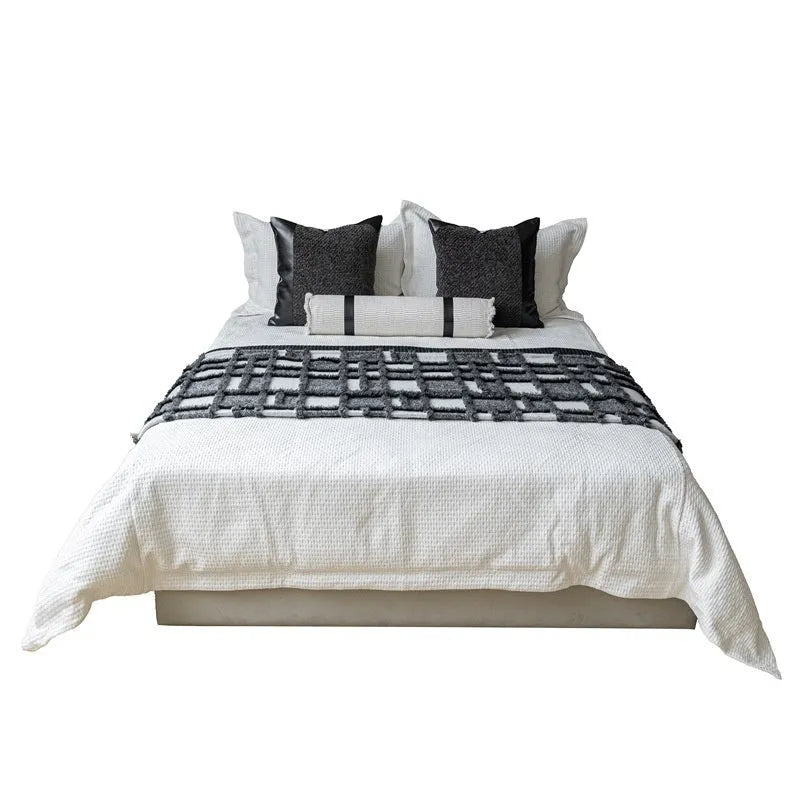 Grey and white plaid bed runner blanket with matching pillowcase and round leather-look pillow on a bed.