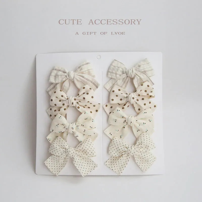 Set of eight children's cloth bow hair clips in various colours including beige polka dot, pink, blue floral, and wine red plaid patterns.