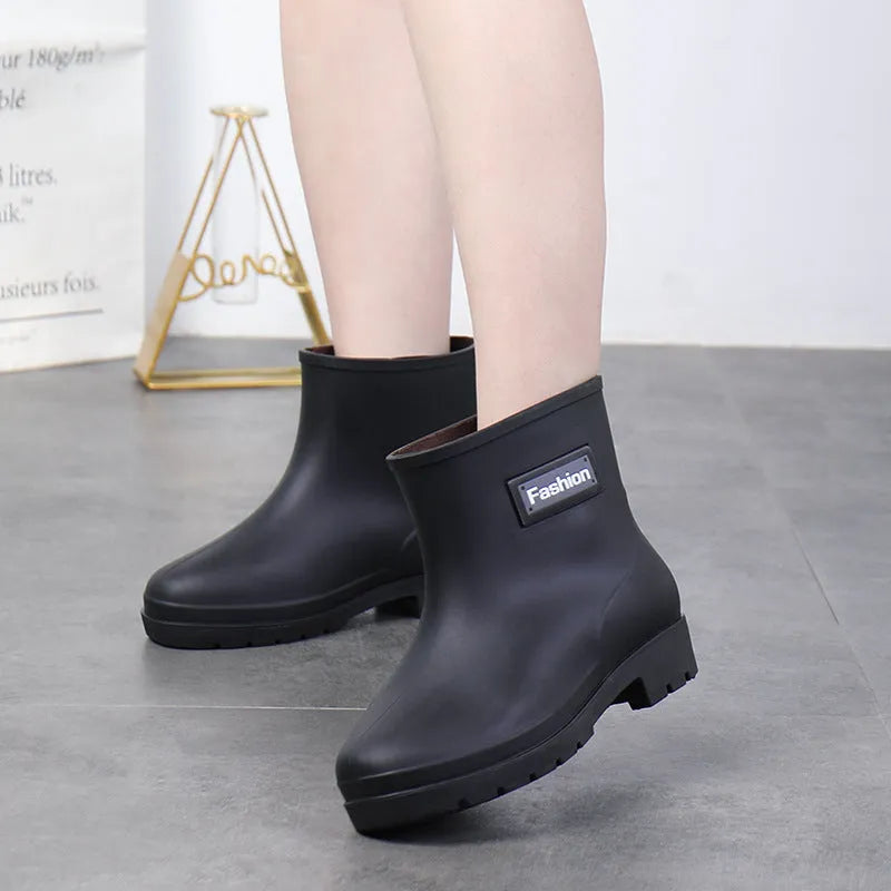 Women's black PVC mid-calf rain boot with a low heel on a wet surface.