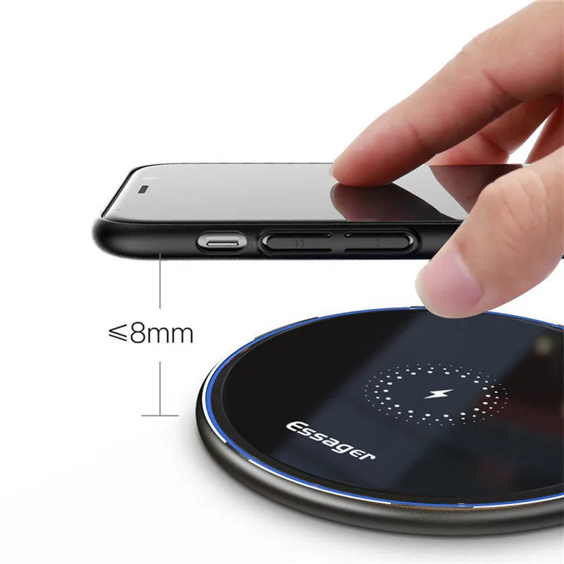 Black Qi fast wireless charging pad on a desk next to a smartphone, showing a blue LED charging indicator light.