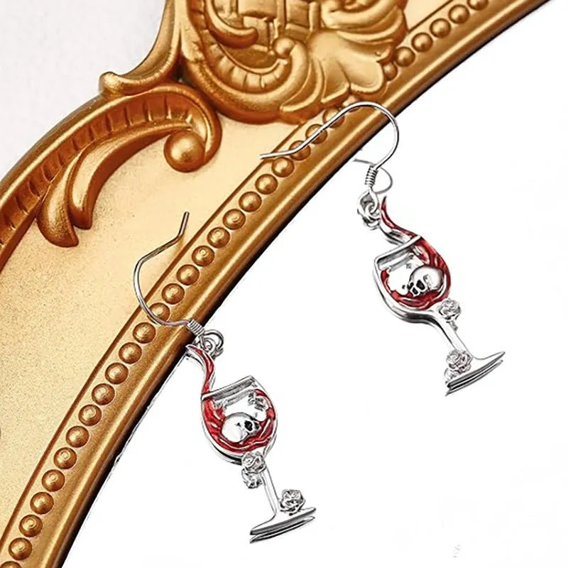A pair of silver-toned zinc alloy earrings shaped like wine glasses adorned with skull details, on a plain background.