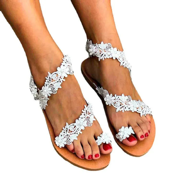 White women's flat sandals with floral pattern and rhinestone decoration on a low slip-on shoe.