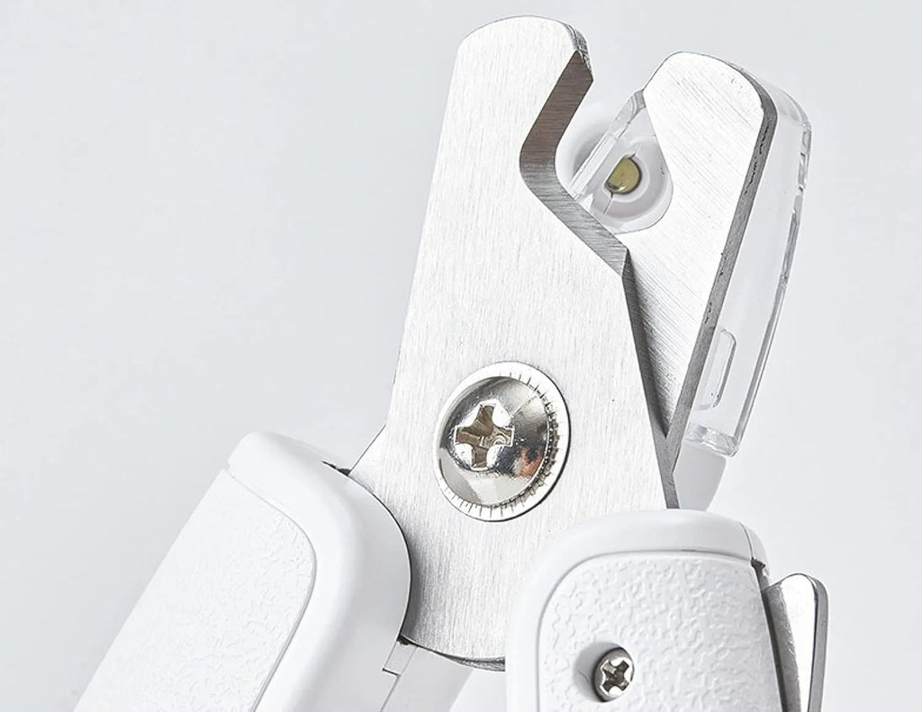 White pet nail clippers with LED light, transparent guard, and leather-like handle next to a nail file.