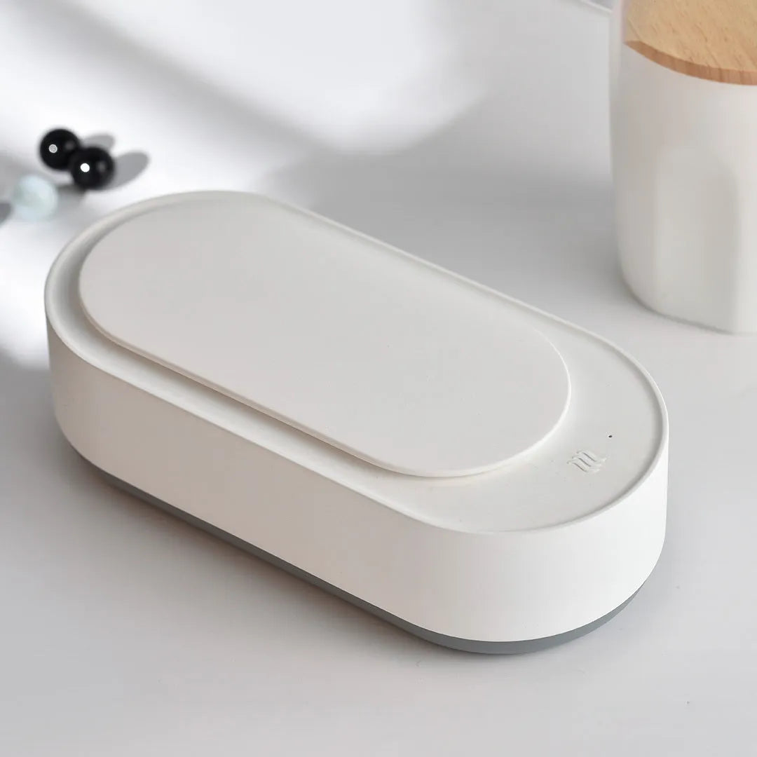White portable ultrasonic cleaner with touch button next to jewellery and glasses on a table.
