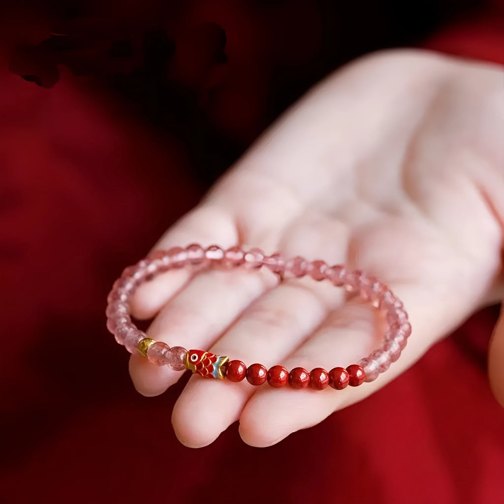 Purple cinnabar and strawberry quartz bracelet with peach blossom and koi charms on a wrist.