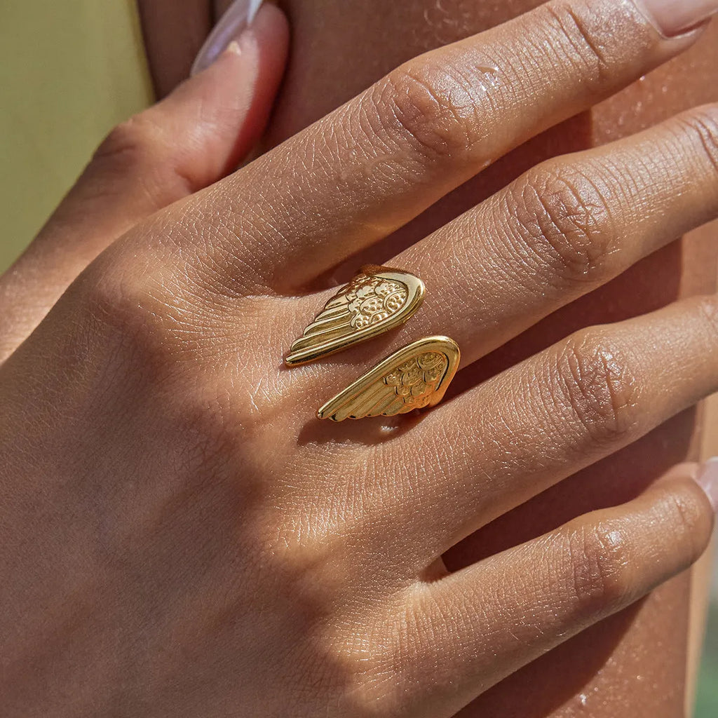 Stainless steel wings ring with an opening design on a plain background, showing wing detail and metallic finish.