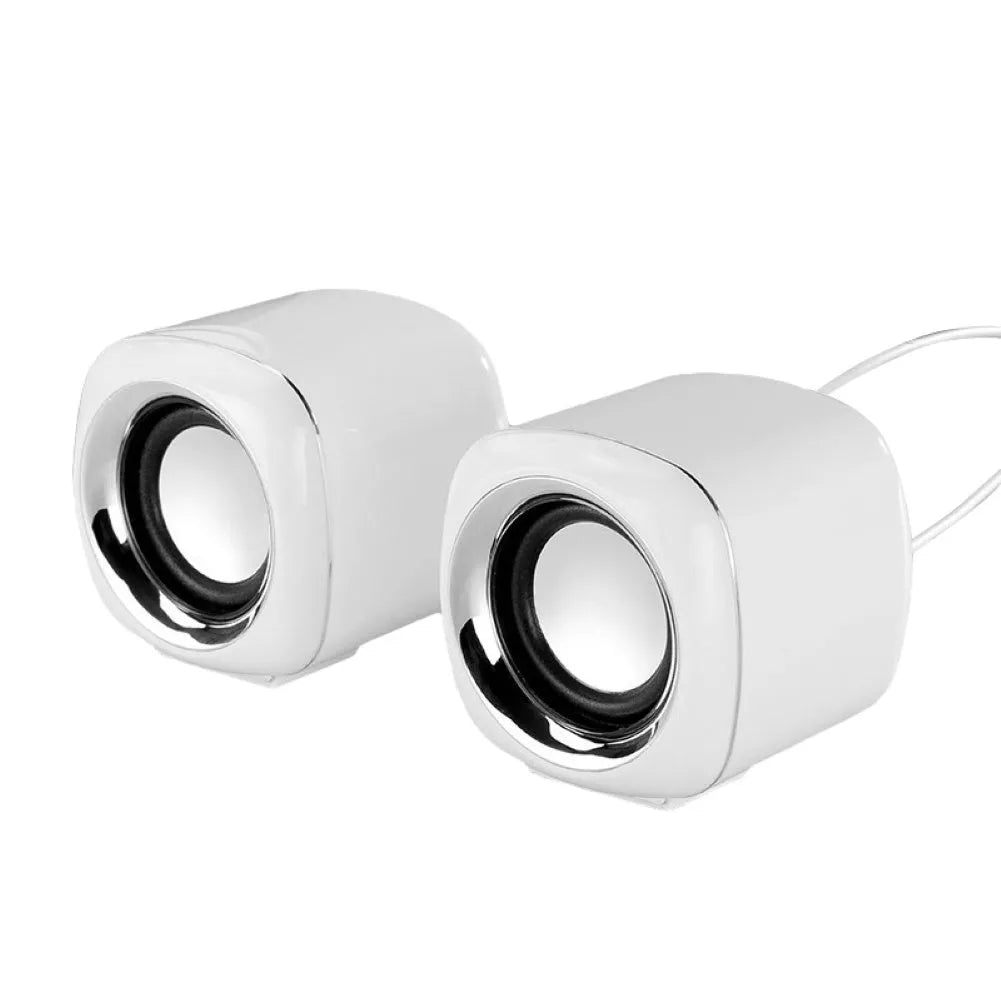 A pair of small black wired computer speakers on a desktop next to a laptop.