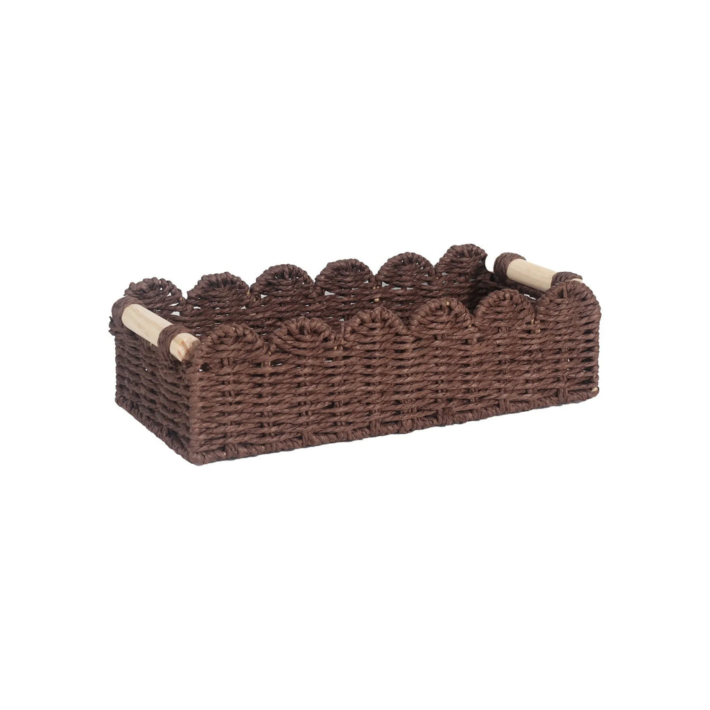 Woven paper storage basket in khaki colour on a wooden desk holding remote controls and pens.