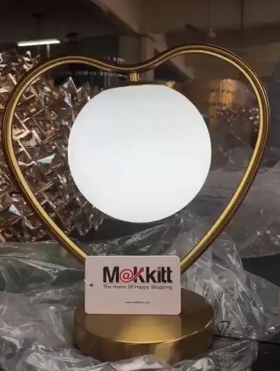 Transparent acrylic heart shaped table lamp with USB cable and dimmer switch on a table.
