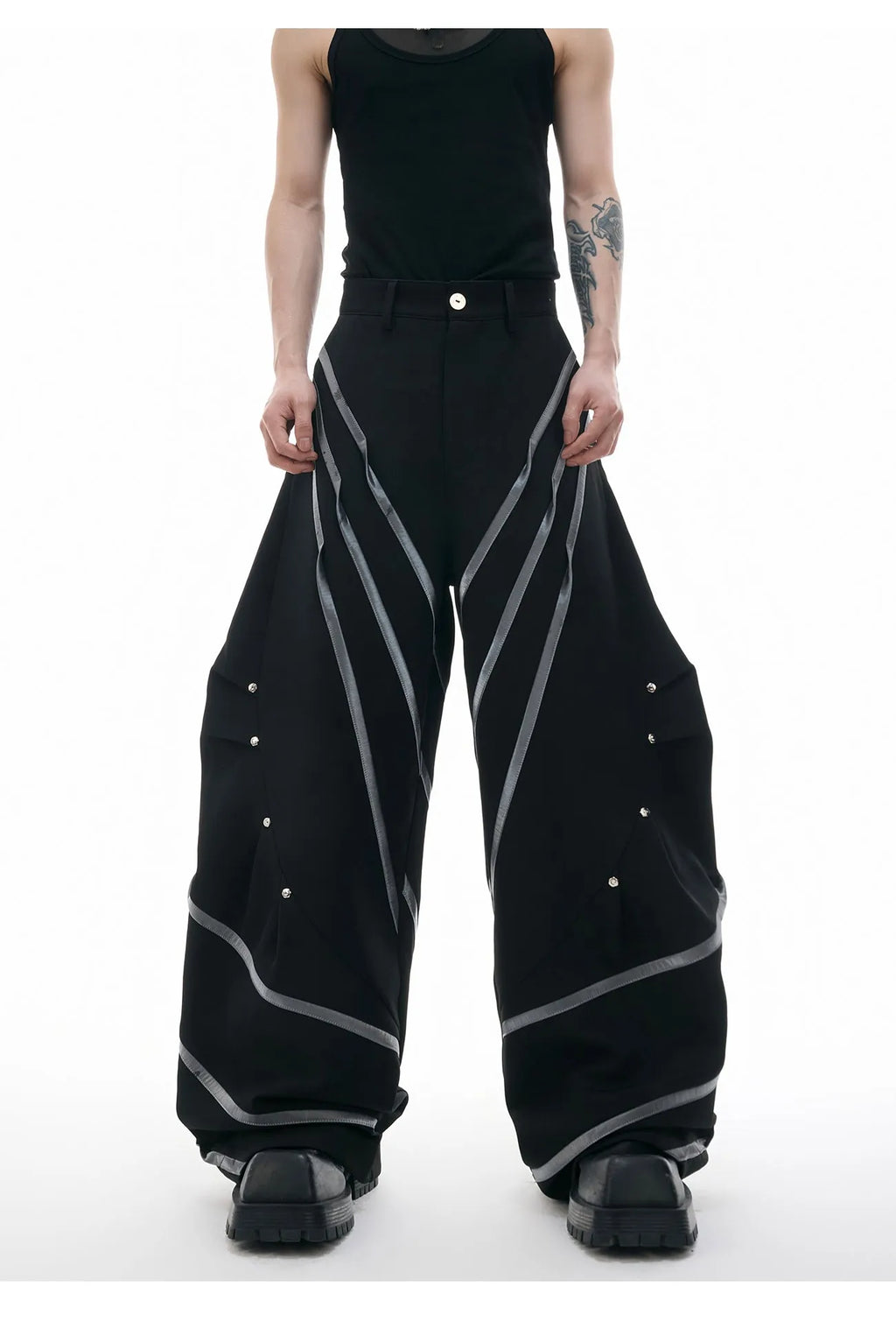 Men's black trousers with three-dimensional cutting, metal striped rivets, and pleated detailing on a hanger.