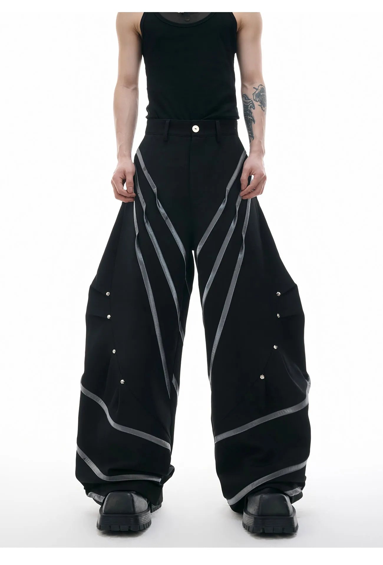 Men's black trousers with three-dimensional cutting, metal striped rivets, and pleated detailing on a hanger.