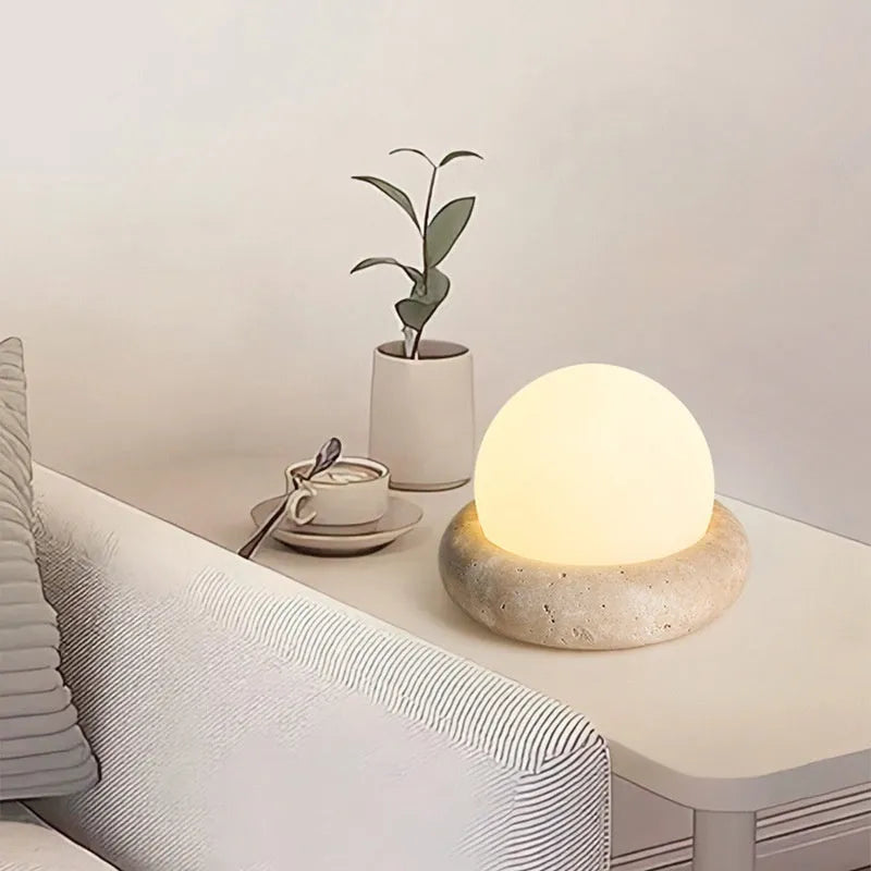 Cream coloured spherical bedside night lamp with remote control on wooden table
