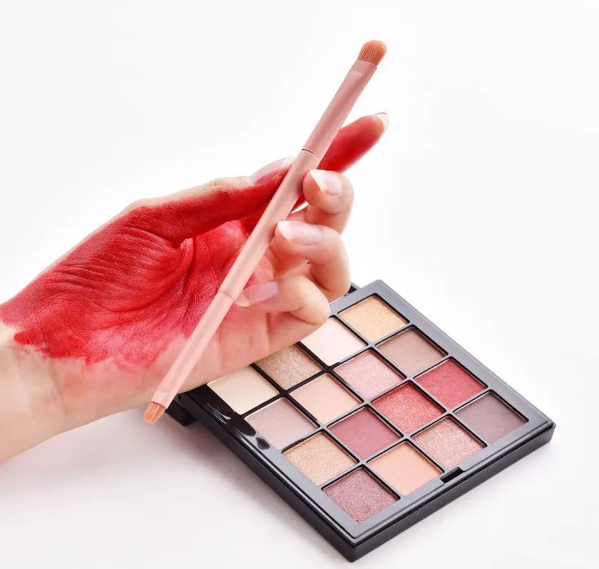 Ten wooden-handle make-up brushes for face and eye application in a pink travel case.