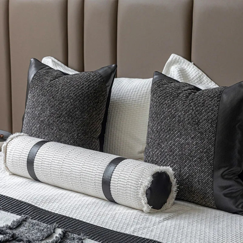 Grey and white plaid bed runner blanket with matching pillowcase and round leather-look pillow on a bed.
