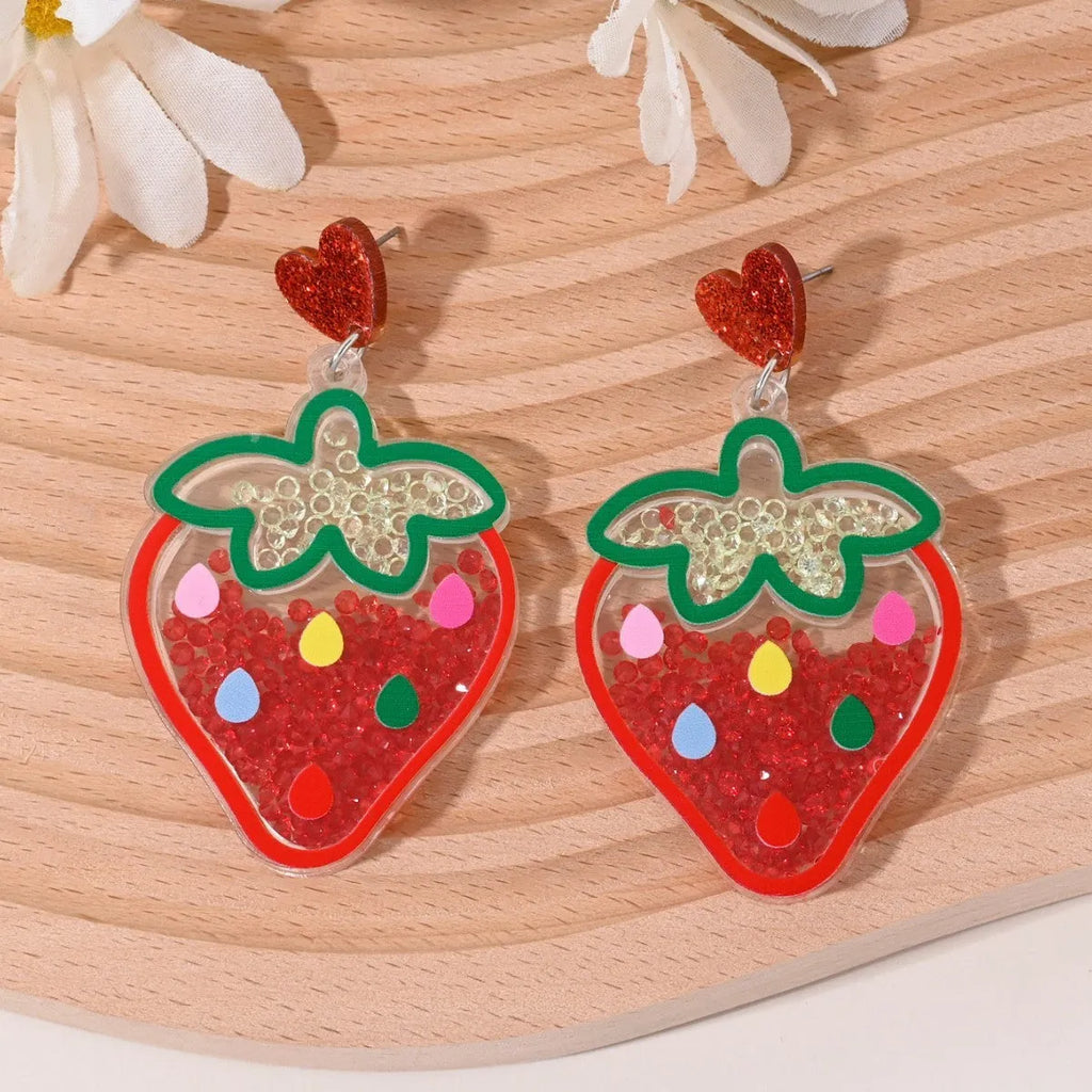 A pair of colourful acrylic earrings with a cake design next to other fruit and ice cream style earrings.