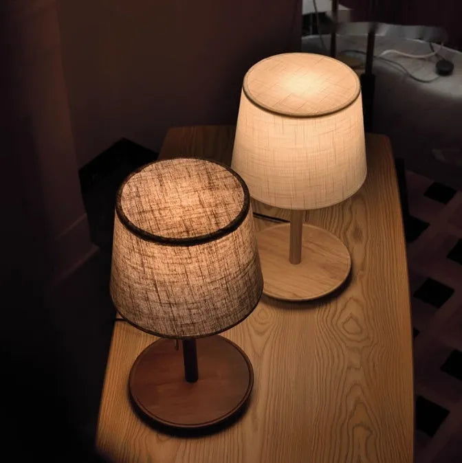 Walnut coloured solid wood bedside lamp with a white cloth shade on a wooden table.