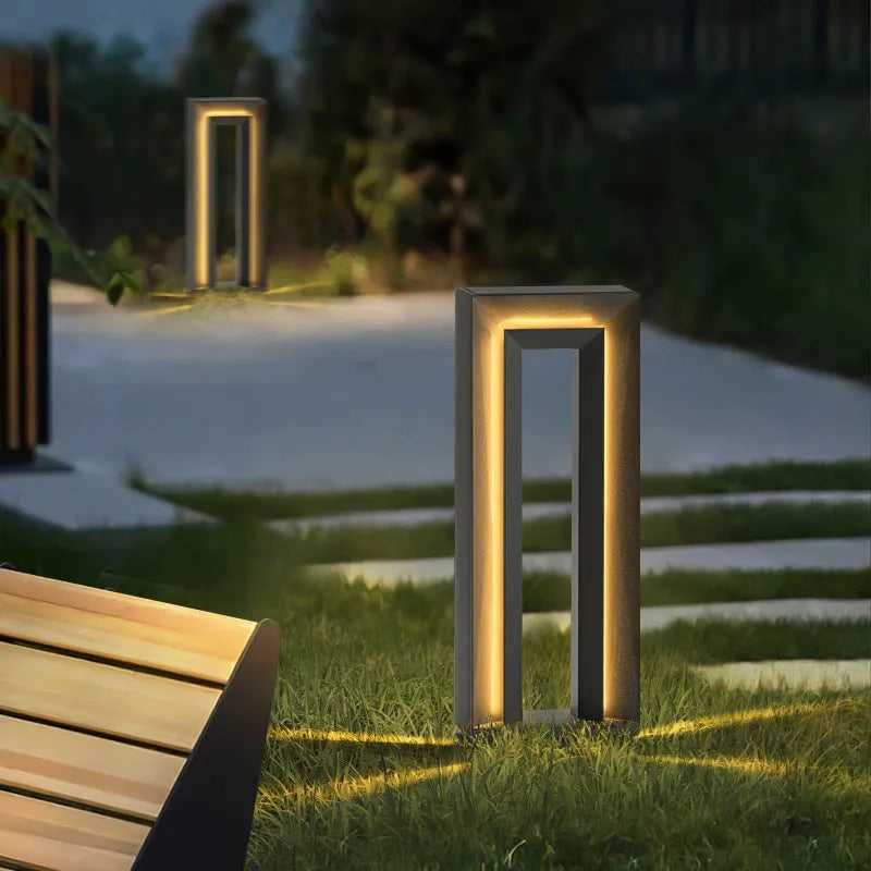 Modern square stainless steel outdoor garden lamp with geometric design on a patio.
