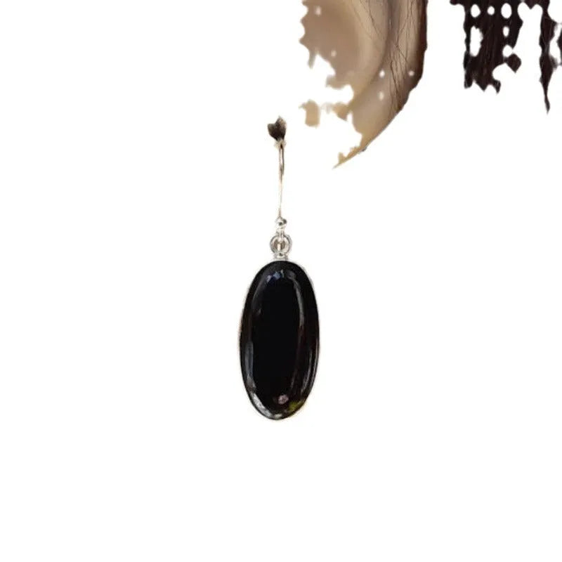 Close-up of women's geometric earrings with oval black agate pendant in silver electroplated setting.