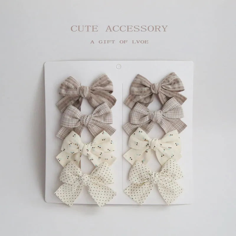 Set of eight children's cloth bow hair clips in various colours including beige polka dot, pink, blue floral, and wine red plaid patterns.