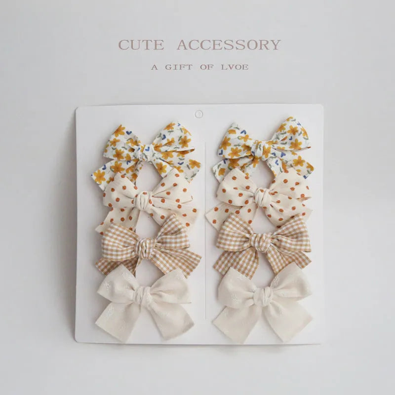 Set of eight children's cloth bow hair clips in various colours including beige polka dot, pink, blue floral, and wine red plaid patterns.