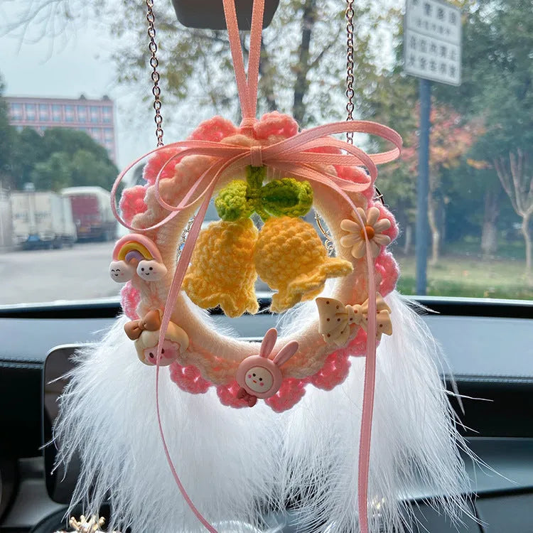 Handwoven wool bell orchid flower car pendant on a green background.