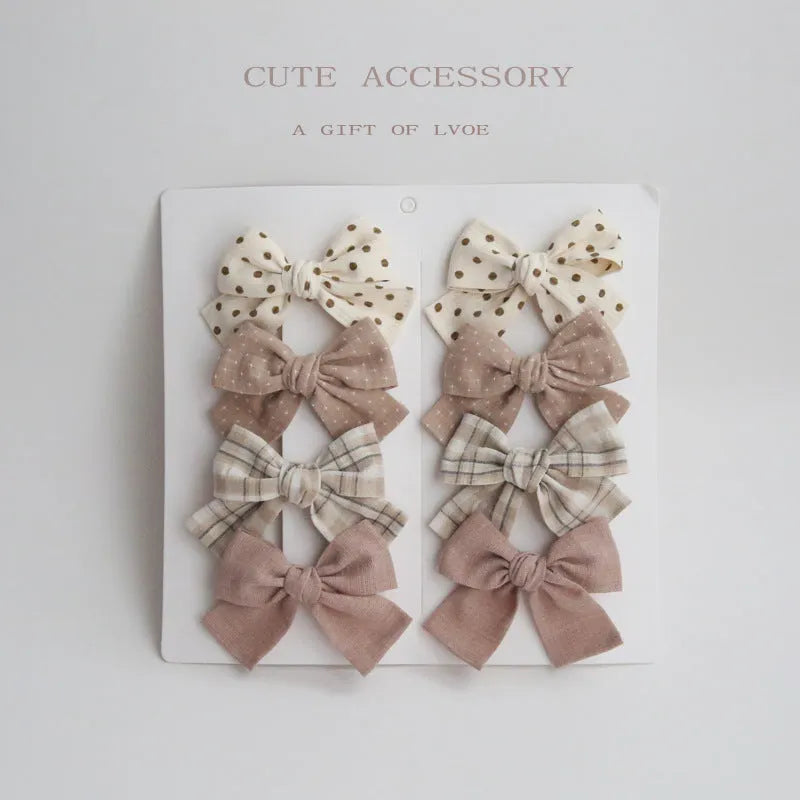 Set of eight children's cloth bow hair clips in various colours including beige polka dot, pink, blue floral, and wine red plaid patterns.