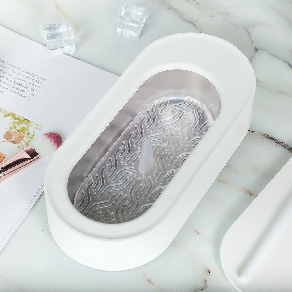 White portable ultrasonic cleaner with touch button next to jewellery and glasses on a table.
