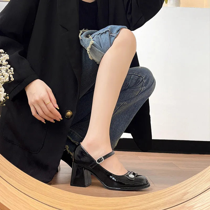 Women's black patent leather round toe high heels with a chunky heel and buckle strap, shown on a foot.