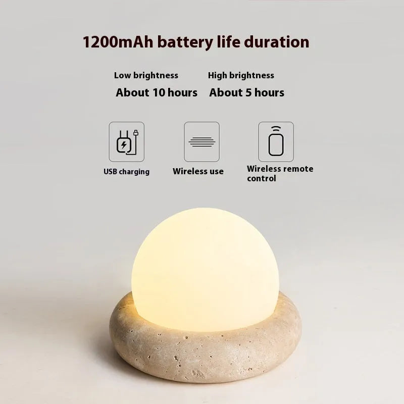 Cream coloured spherical bedside night lamp with remote control on wooden table