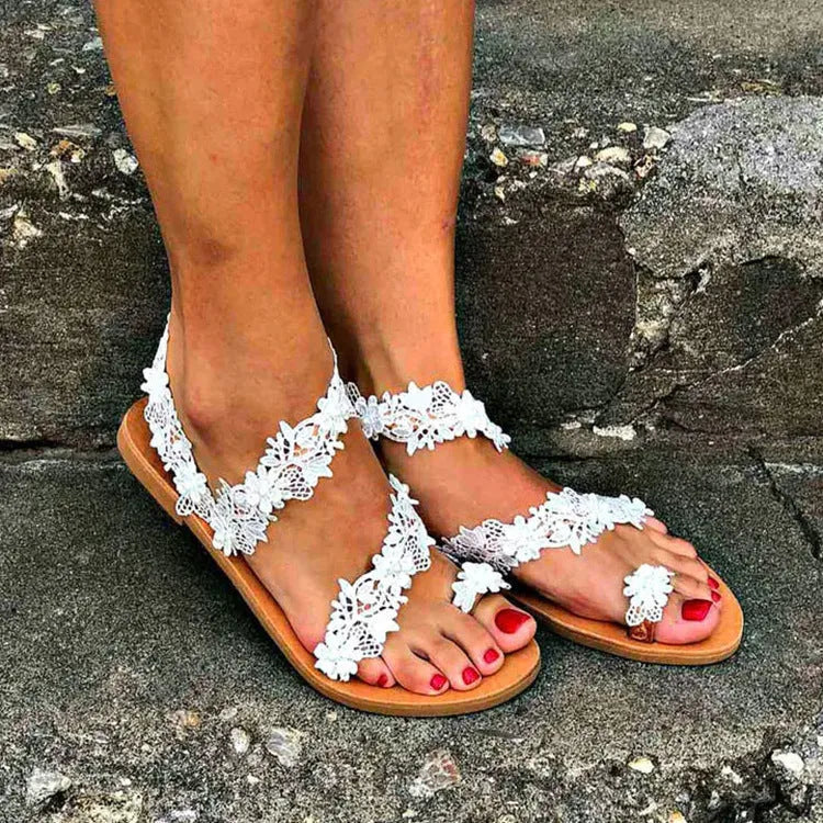 White women's flat sandals with floral pattern and rhinestone decoration on a low slip-on shoe.