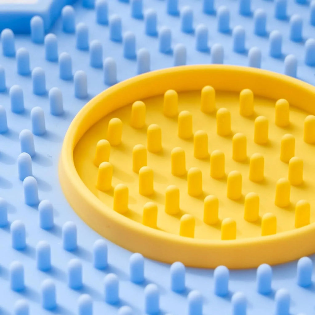 Flower-shaped silicone pet licking mat in blue with suction cups on the back, shown on a tiled surface.