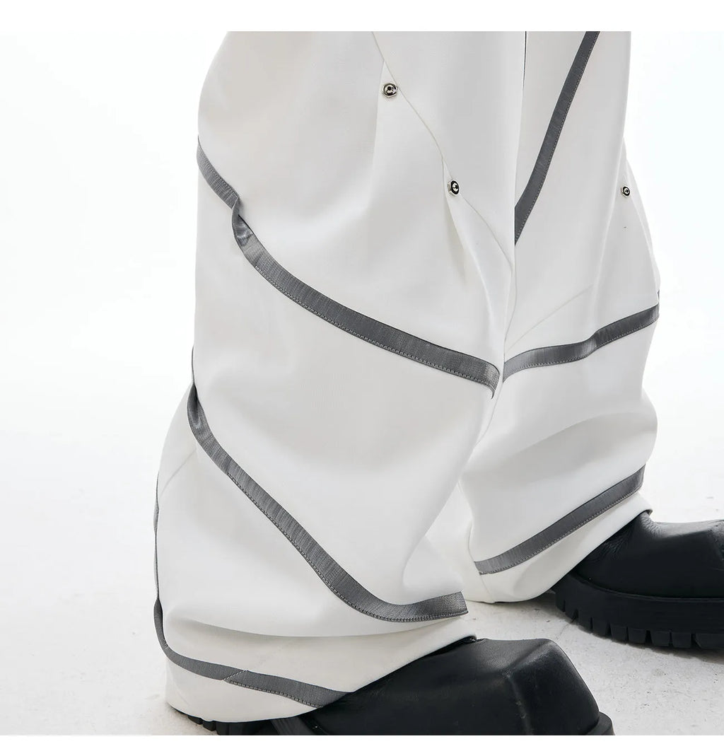 Men's black trousers with three-dimensional cutting, metal striped rivets, and pleated detailing on a hanger.