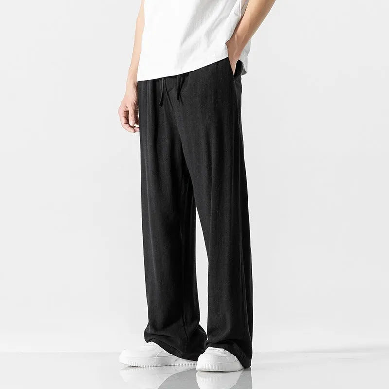 Men's beige linen-style trousers with a loose straight-leg fit and drawstring waist, laid flat.