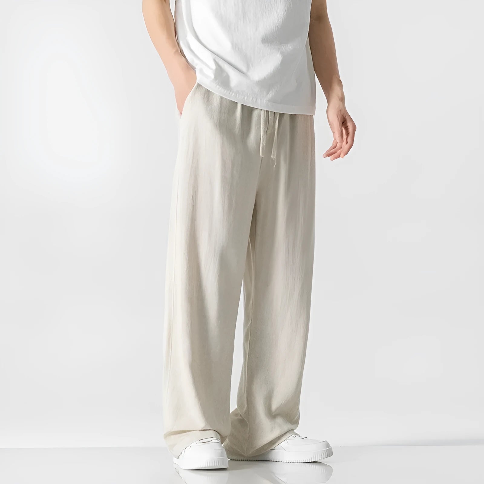 Men's beige linen-style trousers with a loose straight-leg fit and drawstring waist, laid flat.