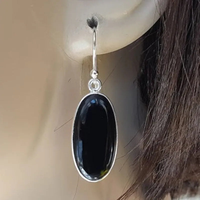 Close-up of women's geometric earrings with oval black agate pendant in silver electroplated setting.