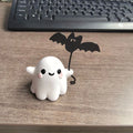 Miniature resin statue of a white ghost dog walking and holding a small black bat, Halloween decoration.