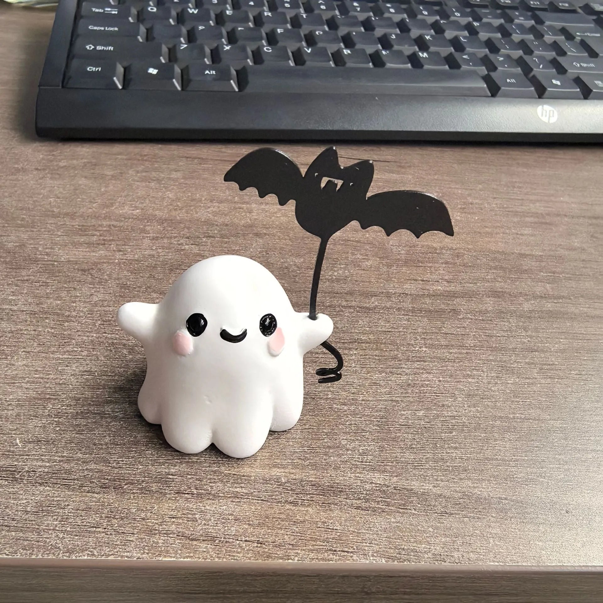 Miniature resin statue of a white ghost dog walking and holding a small black bat, Halloween decoration.