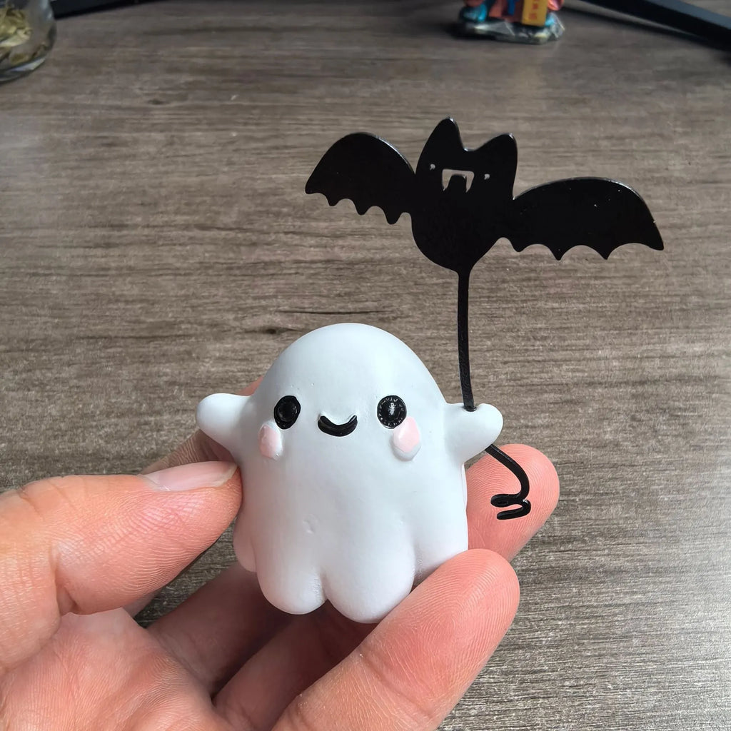 Miniature resin statue of a white ghost dog walking and holding a small black bat, Halloween decoration.