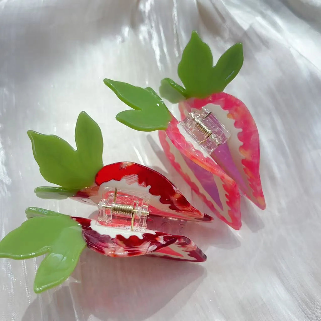 Close-up of a red strawberry-shaped hair clip with a green leaf, on a white background.