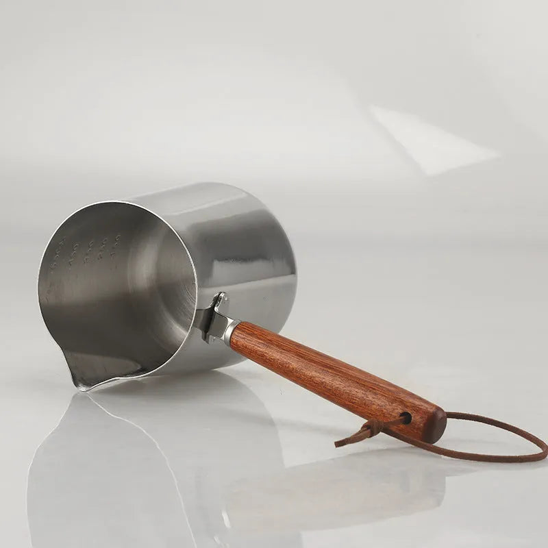 Stainless steel milk jug with wooden handle and internal measuring scale for barista coffee art.