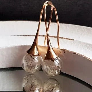 Close-up of transparent glass ball earring with crystal dandelion seed design on a silver hook.