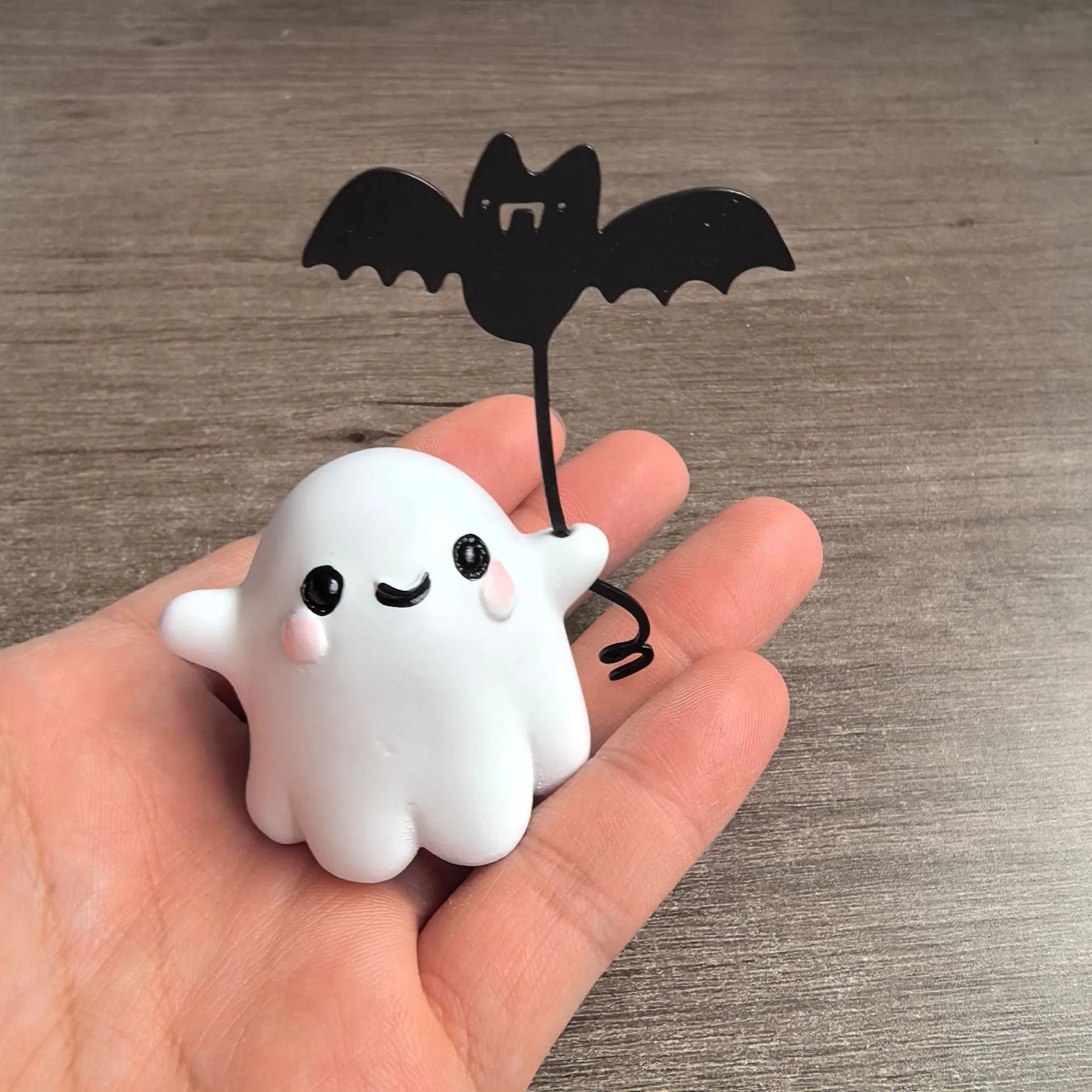 Miniature resin statue of a white ghost dog walking and holding a small black bat, Halloween decoration.