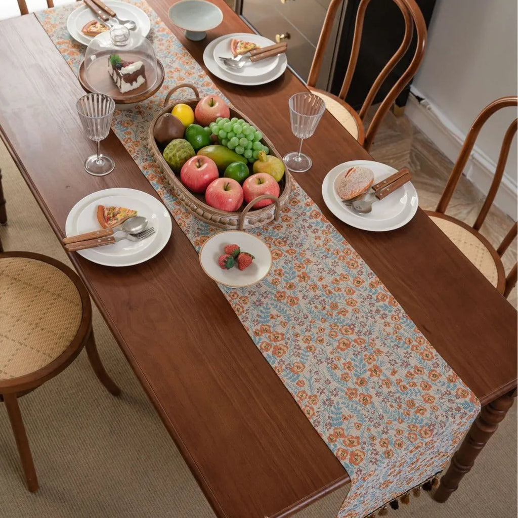Beige jacquard table runner with floral pattern and long tassels laid on a wooden table.