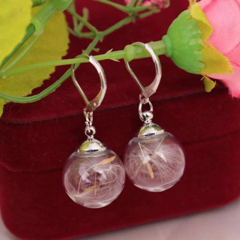 Close-up of transparent glass ball earring with crystal dandelion seed design on a silver hook.