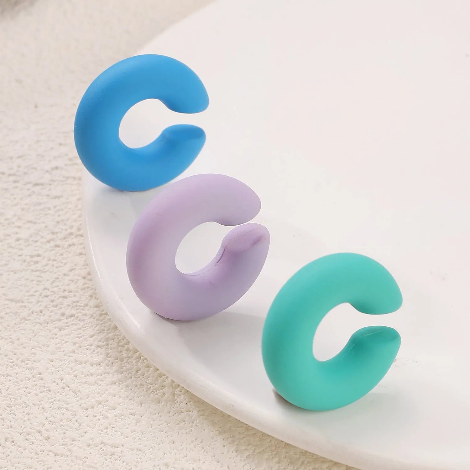 C-shaped clip-on earrings with round geometric shape and matte coarse finish in assorted candy colours.
